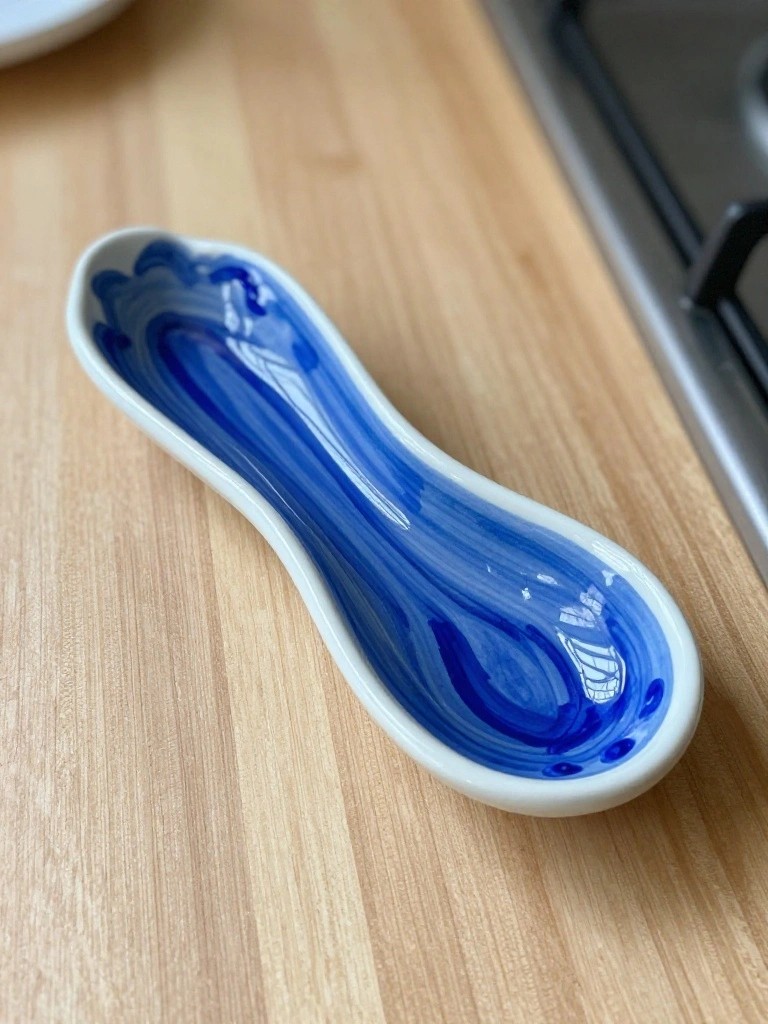 A blue and white wavy-rimmed ceramic dish shaped like an elongated spoon sits on a wooden kitchen counter near a stove.