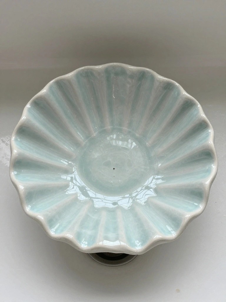 Light blue glossy ceramic bowl with scalloped ruffled edges on a black pedestal base.