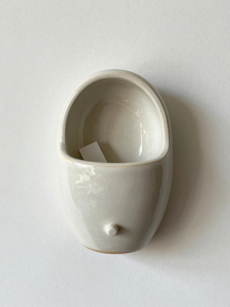 White ceramic wall-mounted holder shaped like a urinal with a small paper tag inside.