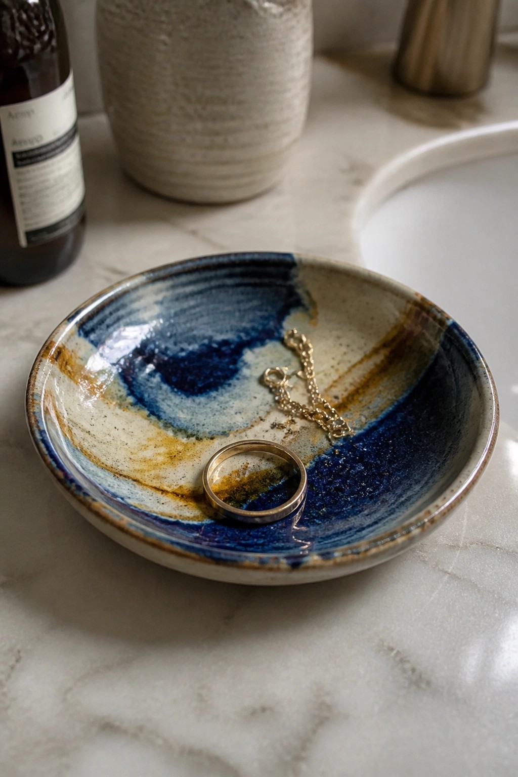 Blue and brown ceramic bowl with gold ring and chain on marble counter