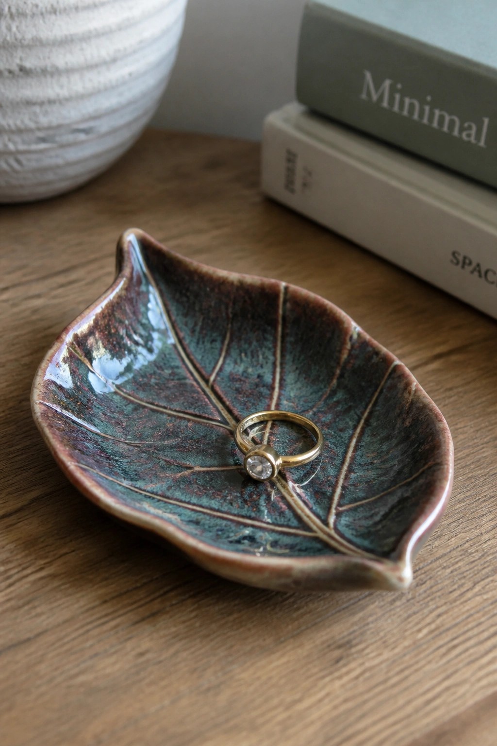 Gold ring with diamond inside green leaf-shaped ceramic dish on wood table