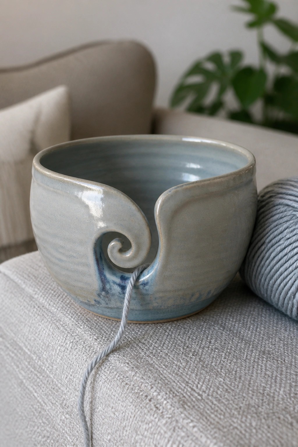 Light blue ceramic yarn bowl with spiral cutout beside gray yarn ball