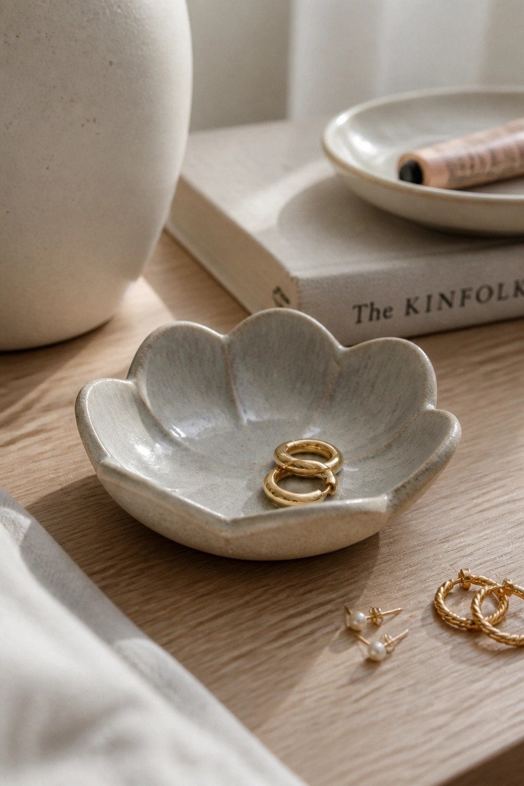 Ceramic flower bowl with gold hoops and scattered pearl earrings on wooden table