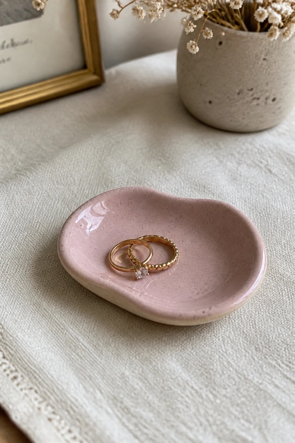 Two gold rings in a pink speckled ceramic dish on white linen.