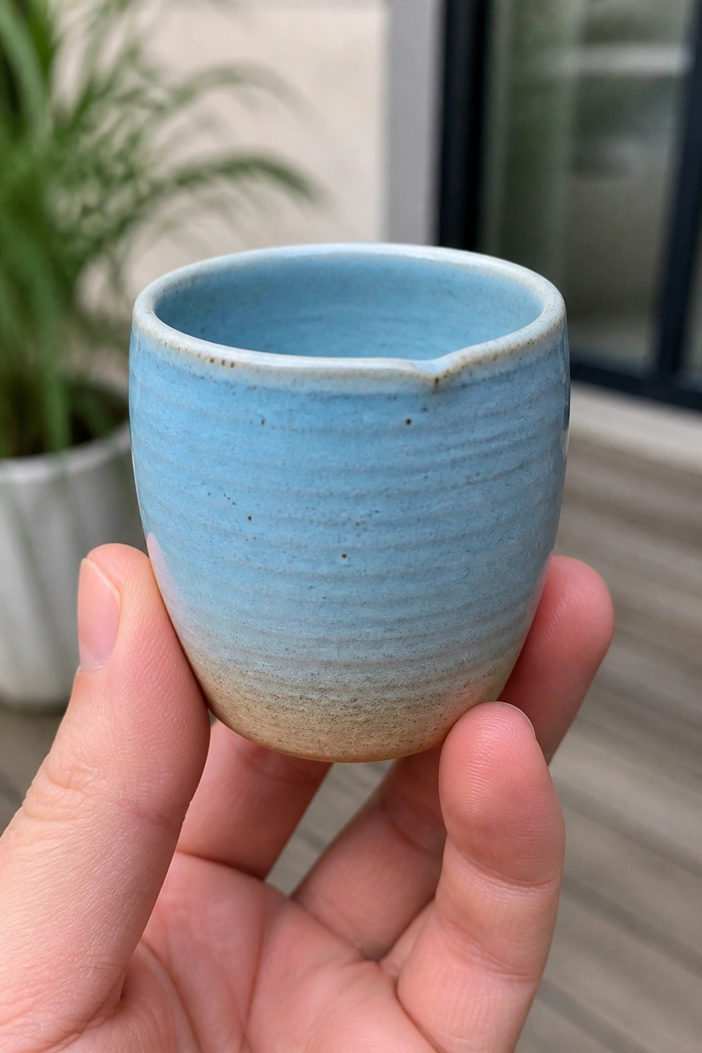 Hand holding small light blue ceramic cup with spout and ridged glaze