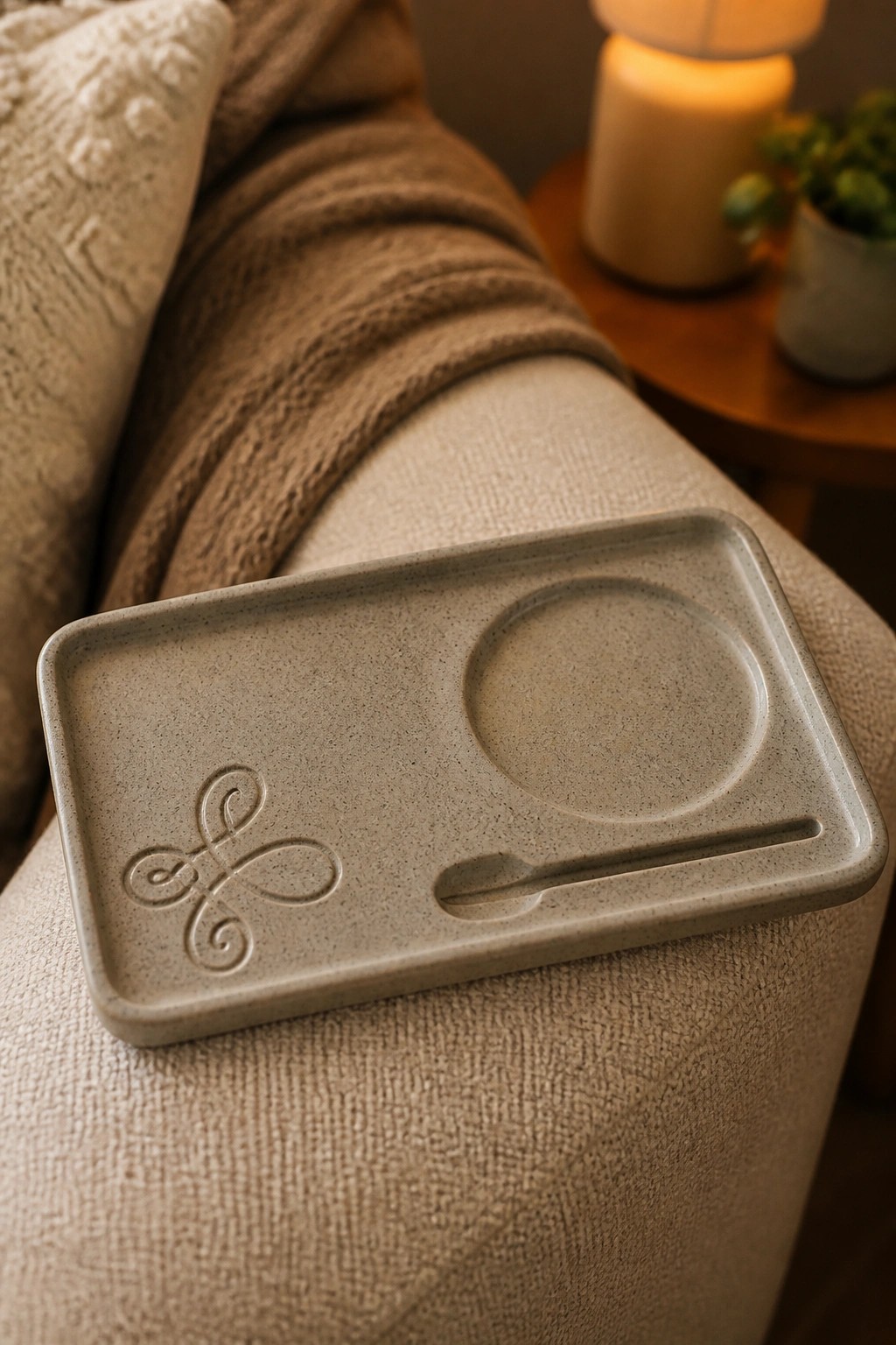 Speckled beige tray with logo, circular well, and spoon slot on textured couch.