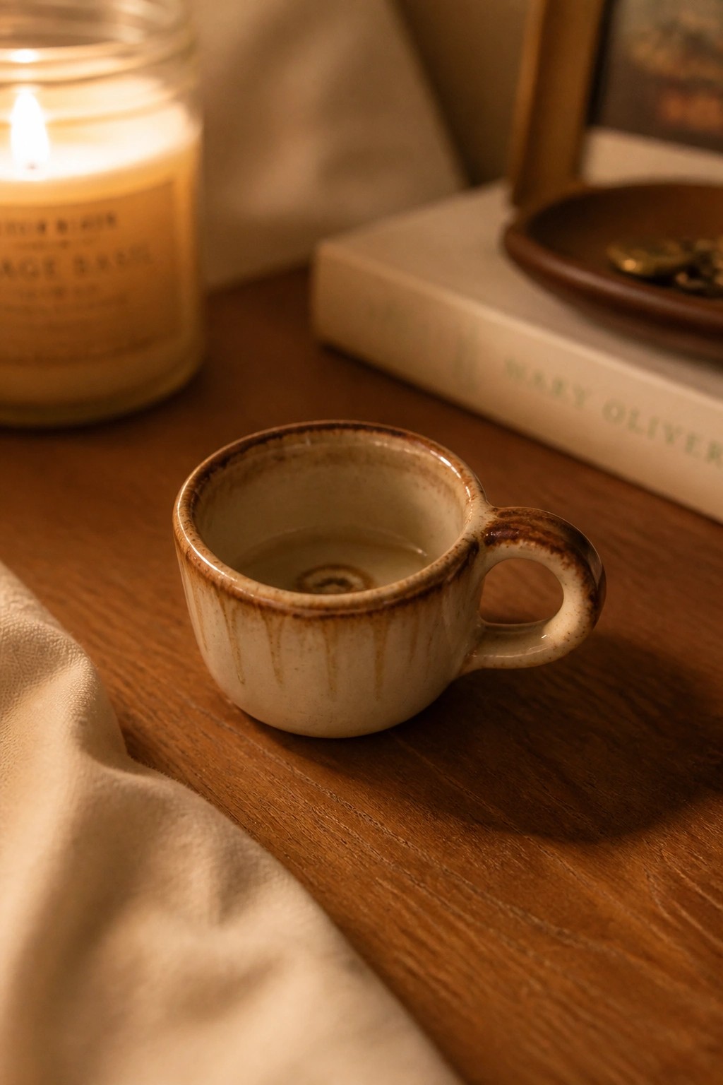 Small ceramic cup with brown glaze on wooden table beside lit candle