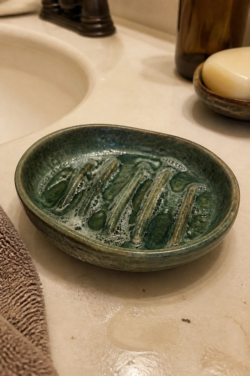 Glossy green ridged soap dish with suds on wet bathroom countertop