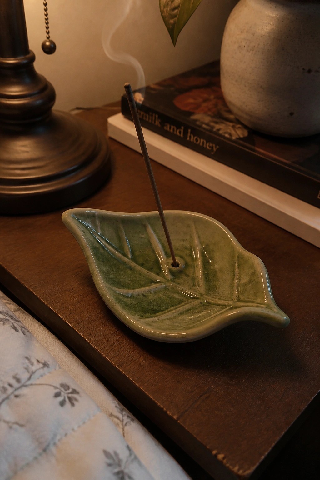 Green leaf-shaped ceramic holder with burning incense stick on wooden table.