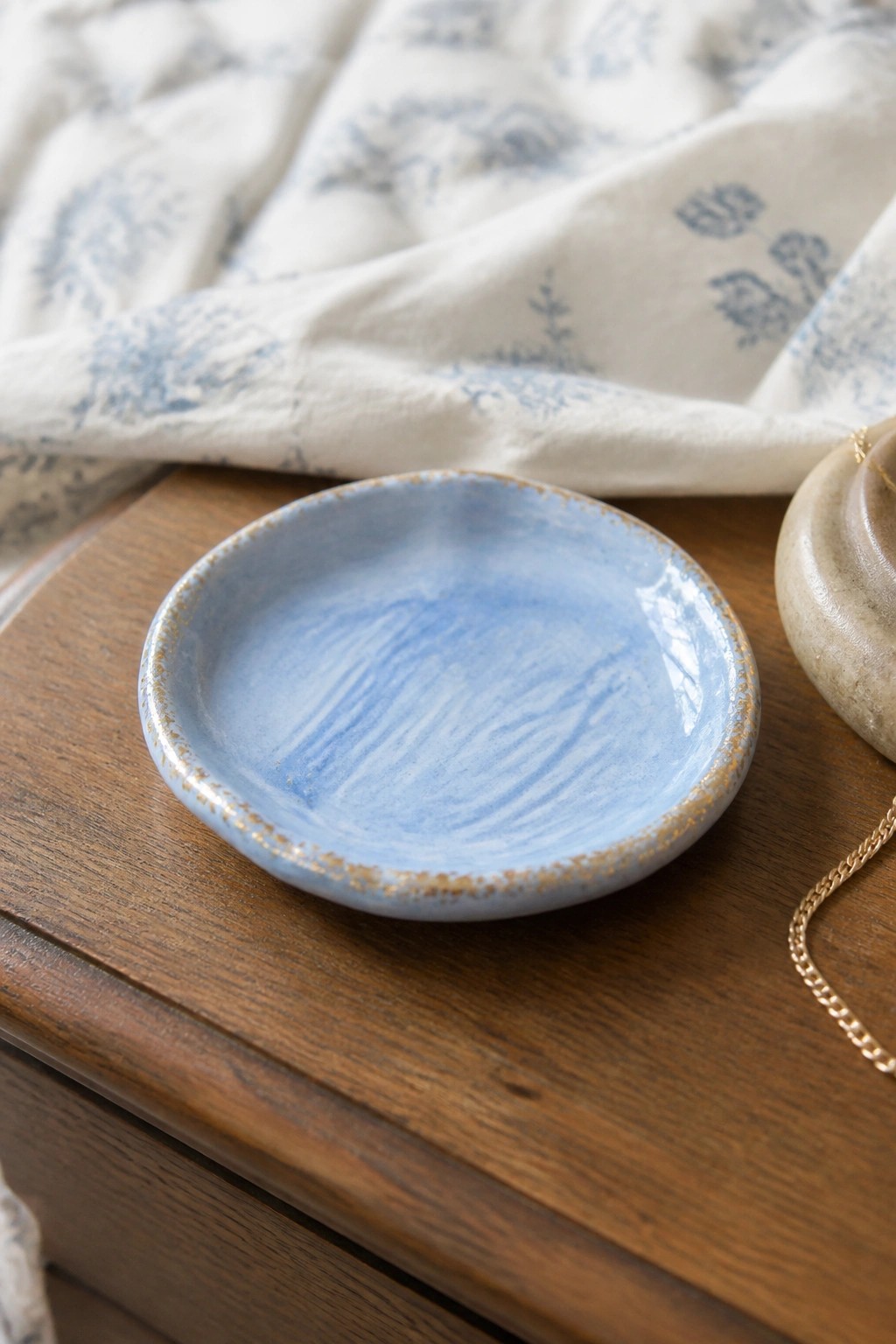 Small blue ceramic dish on wood with white floral cloth and gold chain