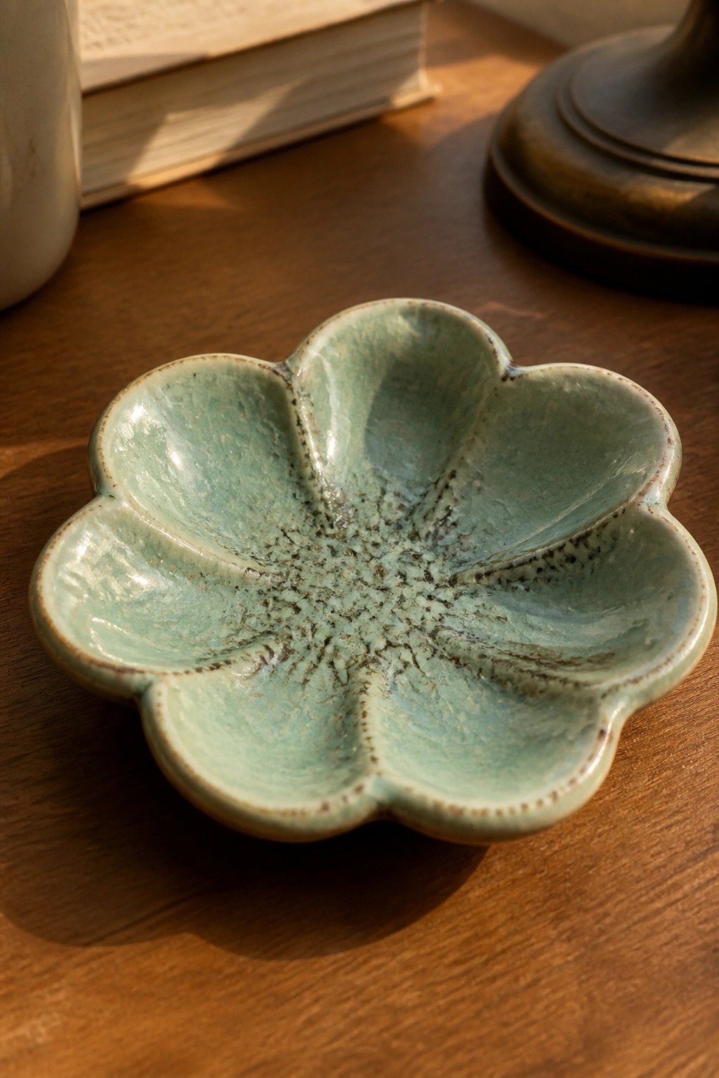 Crackled turquoise ceramic flower-shaped dish on wooden table with books nearby