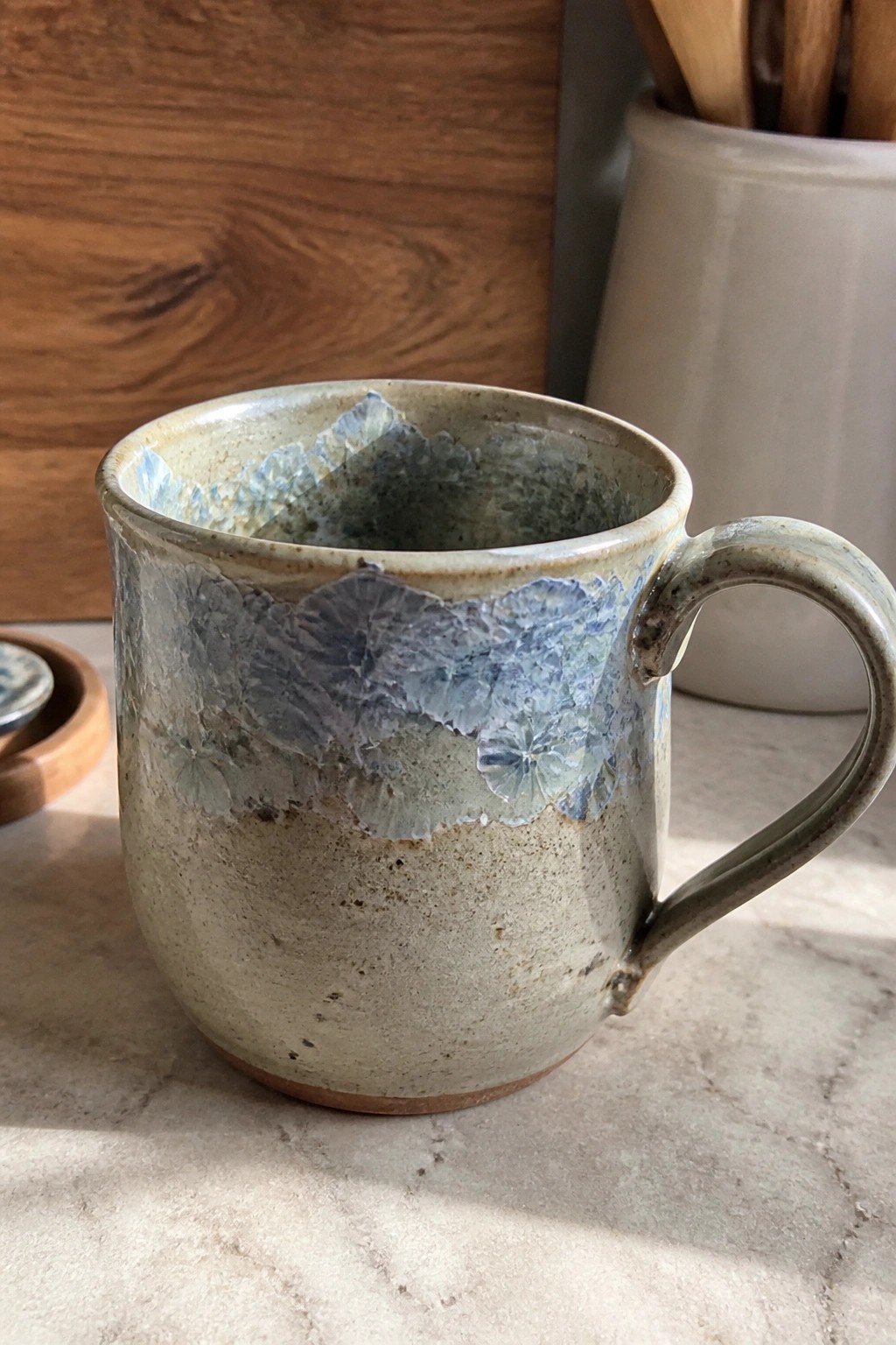 Rustic ceramic mug with blue crystalline glaze and handle on marble counter