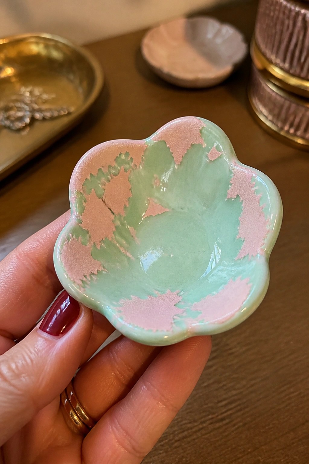 Hand holding pink and green flower-shaped ceramic dish with red nails