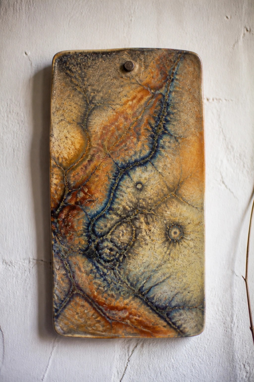 Rectangular ceramic plaque with crackled blue, orange, and brown glaze on white wall