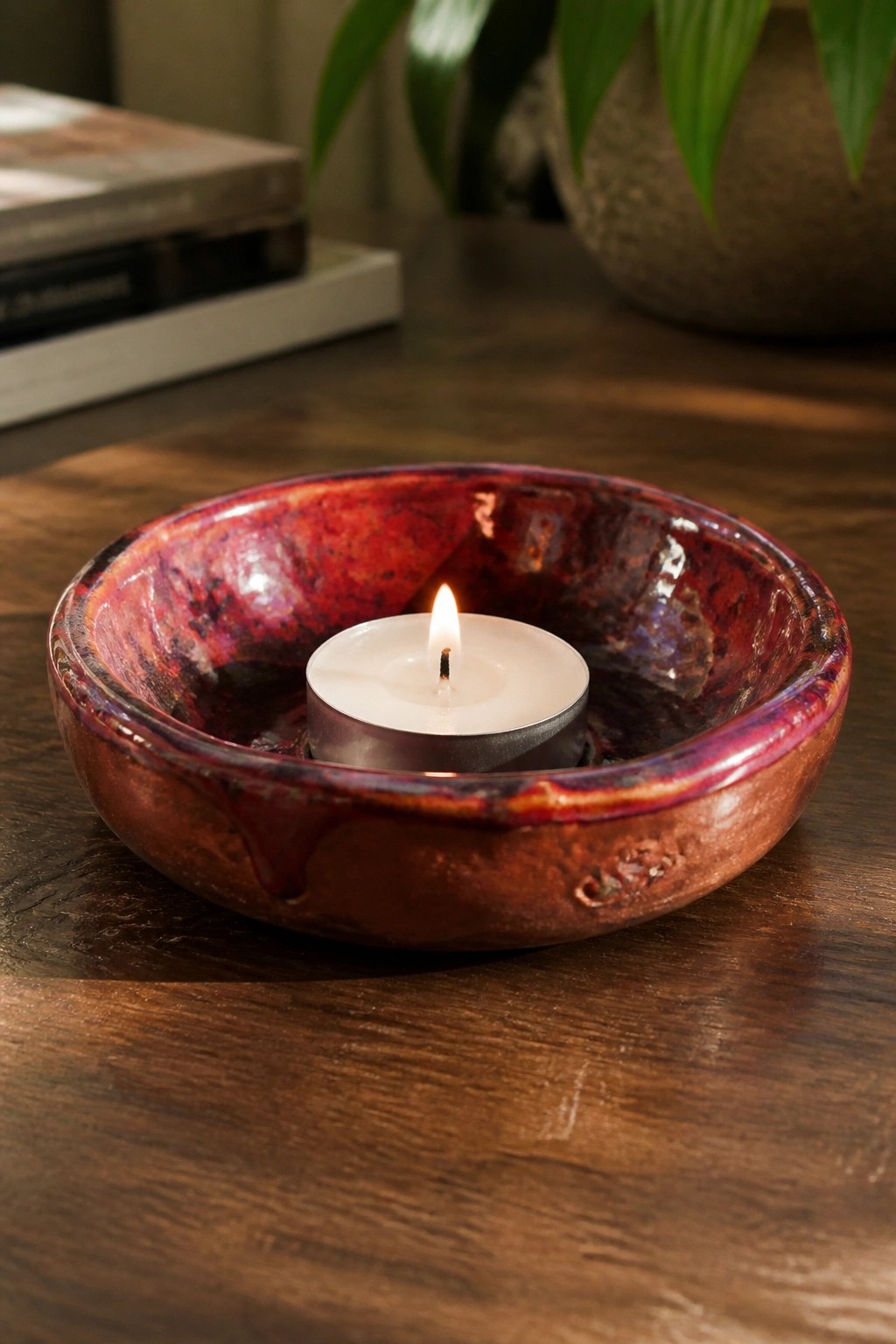 Lit white tealight candle in glossy red-purple ceramic bowl on dark wood