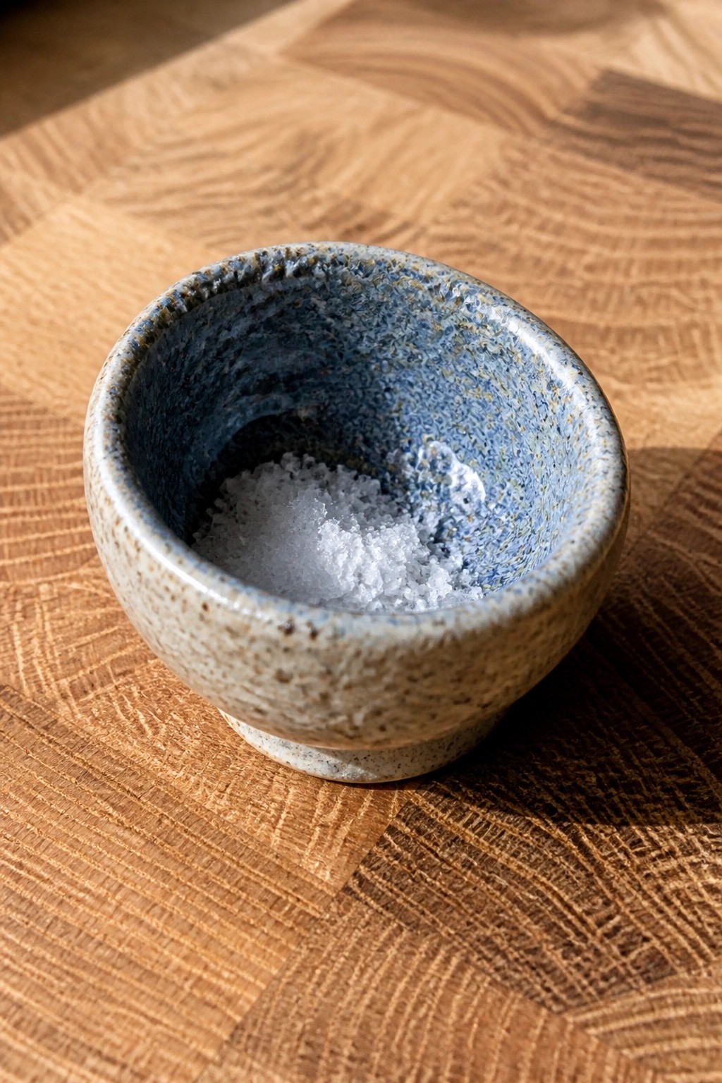 Speckled blue ceramic bowl with white salt on wooden surface