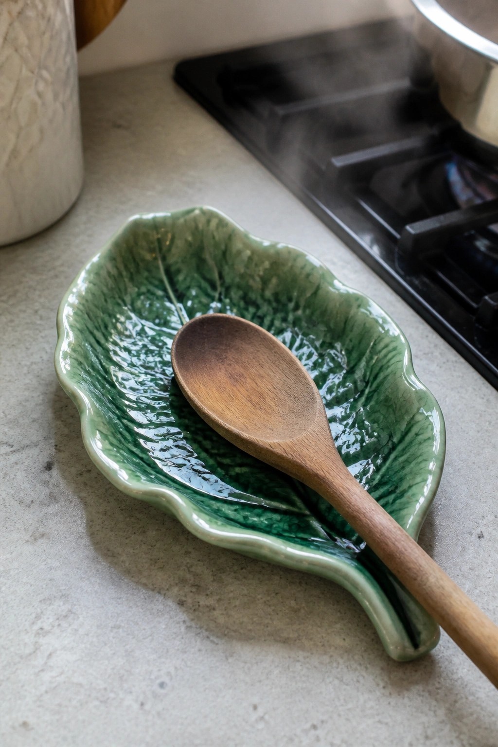 Wooden spoon in glossy green leaf-shaped ceramic dish on kitchen counter