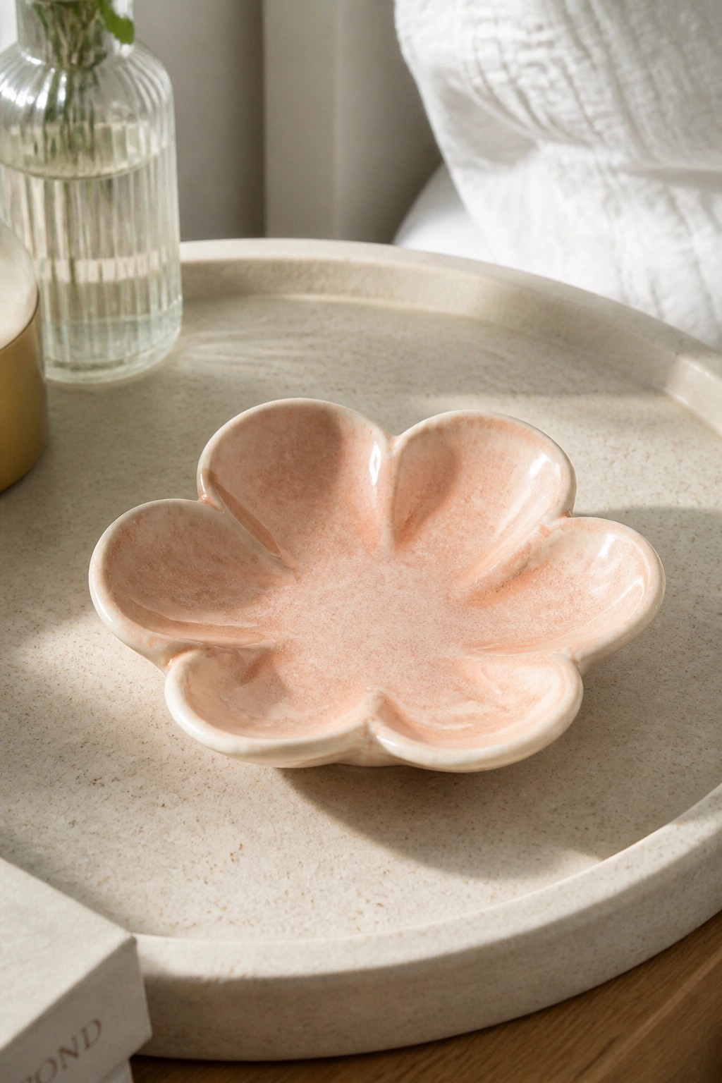Pink flower-shaped ceramic bowl on beige tray beside glass vase.