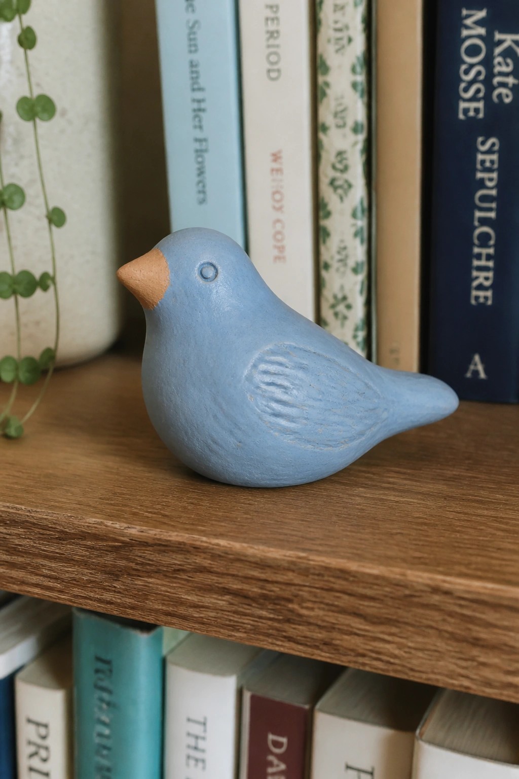 A small blue ceramic bird figurine with a brown beak on a wooden bookshelf.