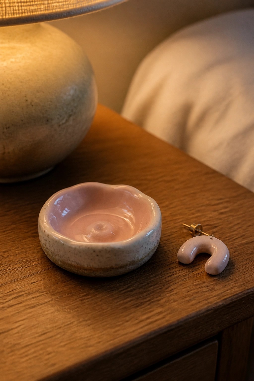 Pink ceramic bowl and C-shaped earring on wooden table beside lamp