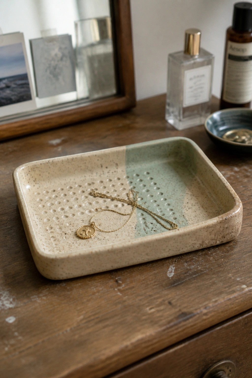Gold necklace with pendant in speckled two-tone ceramic tray on wood.