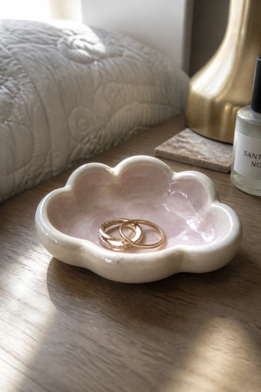 Two gold rings in a pink cloud-shaped ceramic dish on wooden table