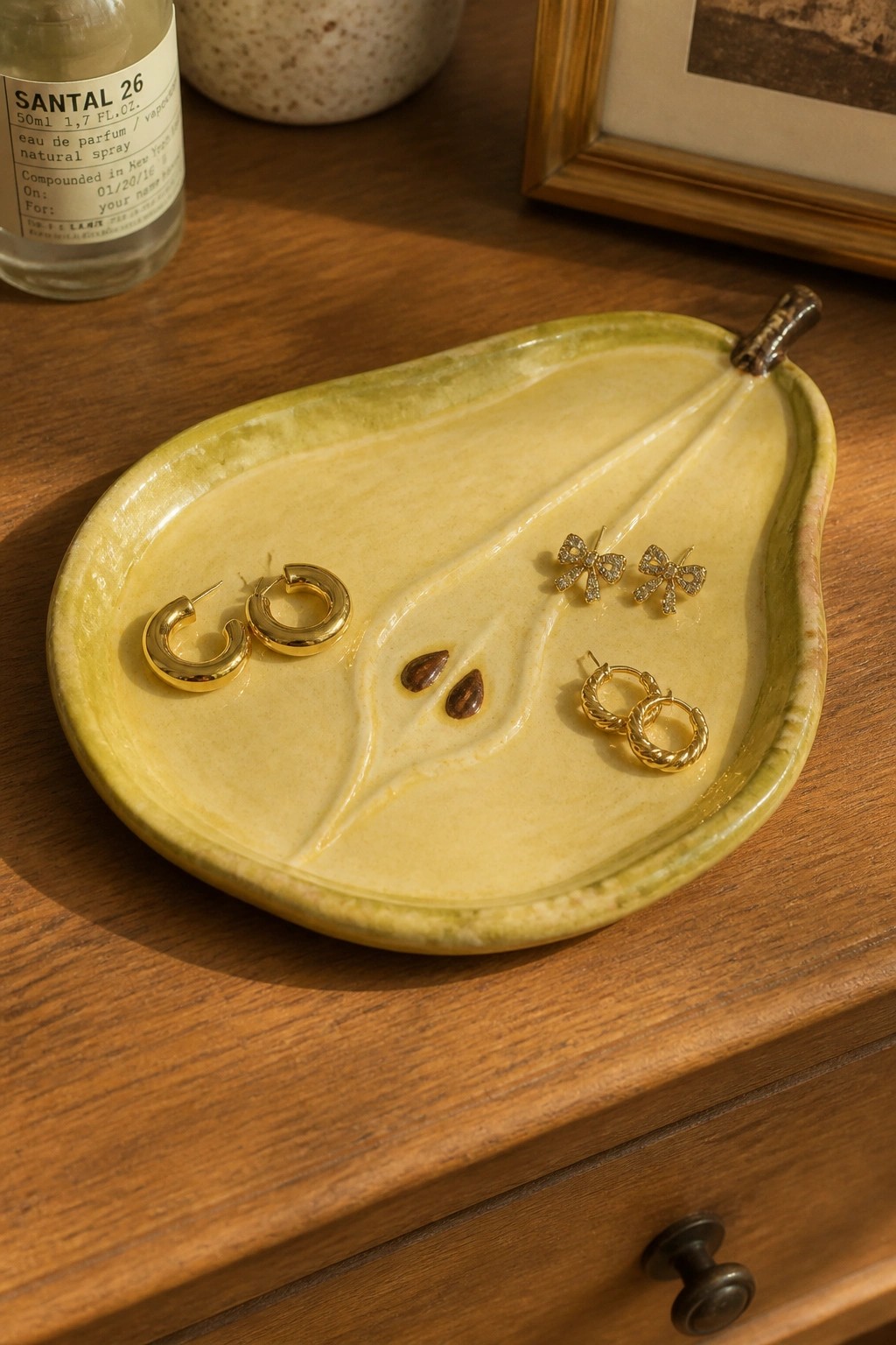 Yellow-green pear-shaped ceramic dish with gold earrings on wooden dresser