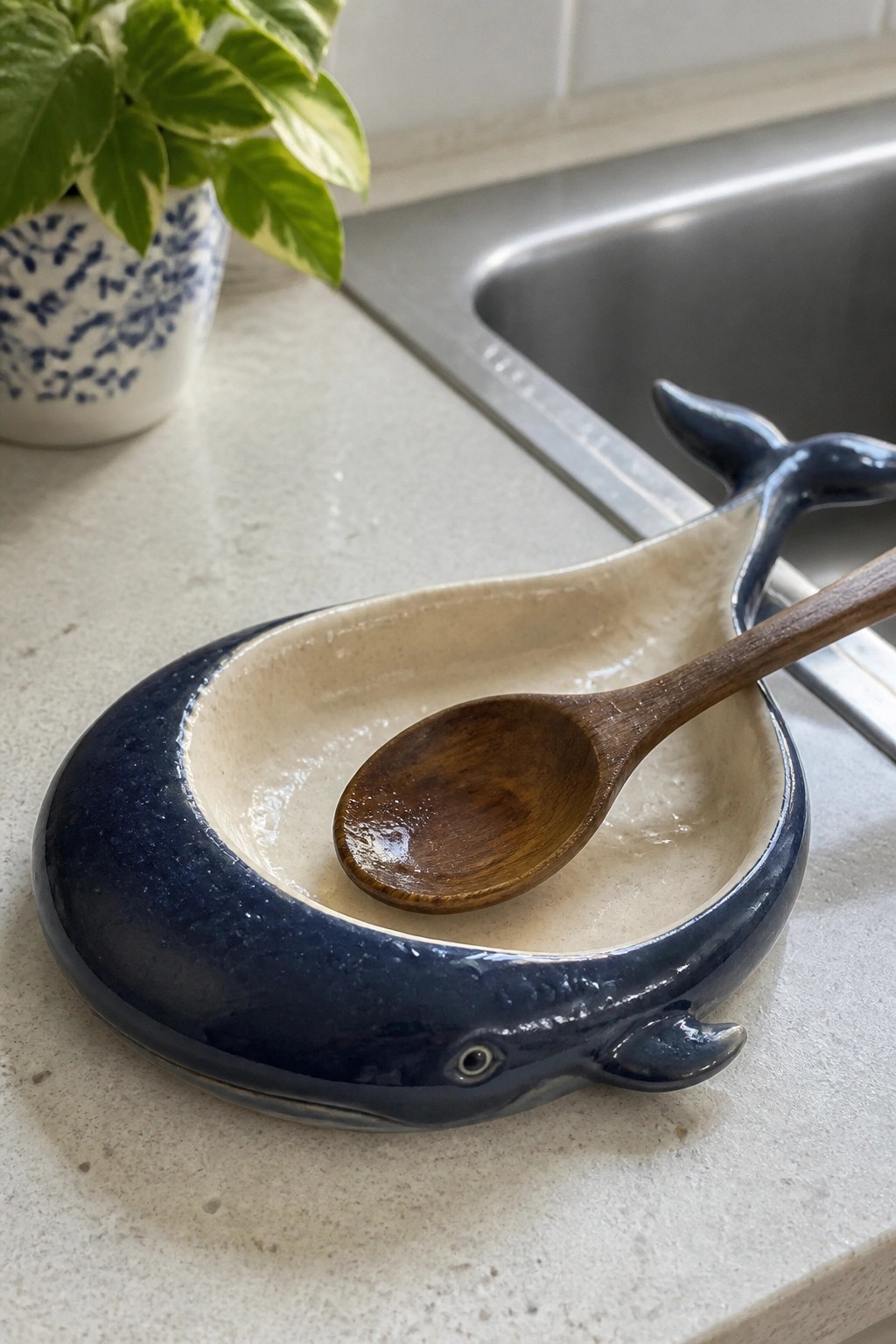Dark blue ceramic whale bowl with wooden spoon on kitchen counter near plant