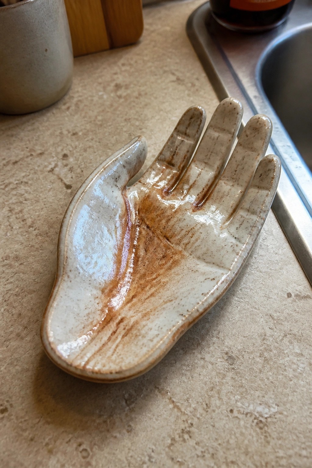 Ceramic dish shaped like an open hand with white and brown glaze on a kitchen countertop.