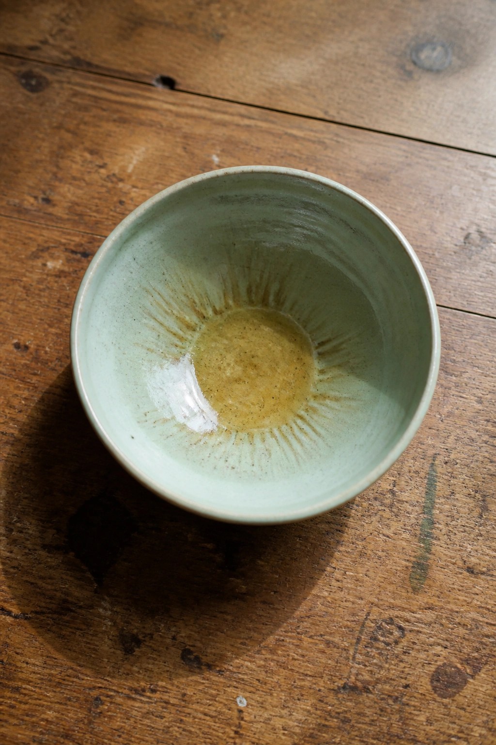 Pale green ceramic bowl with yellowish residue on rustic wooden table