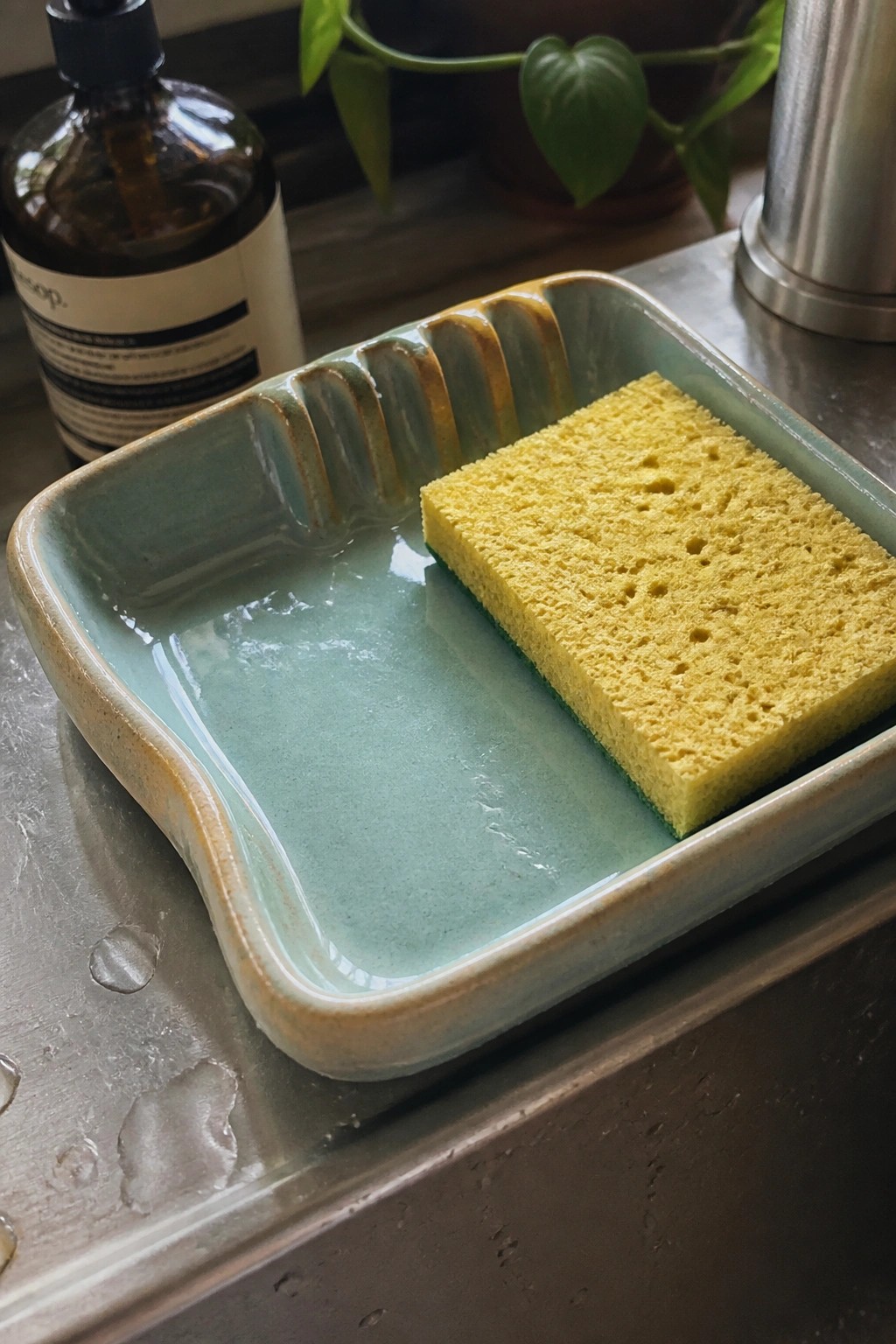 Yellow sponge in a wet light blue ceramic dish on stainless steel sink