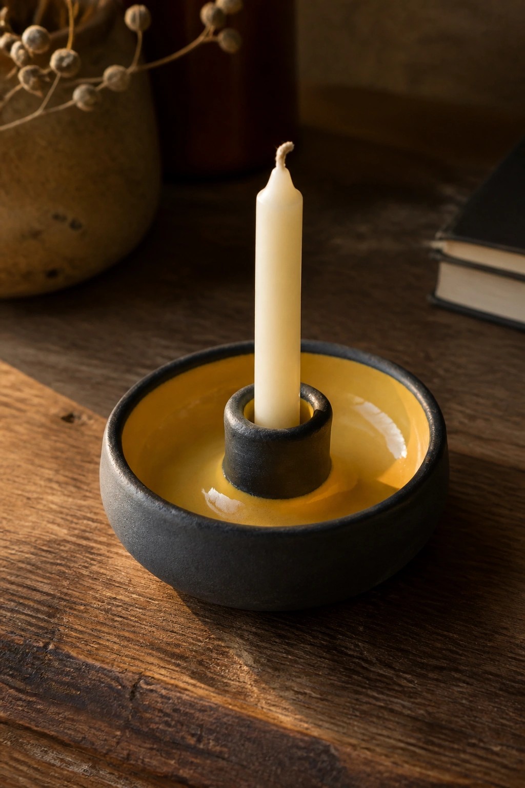 White candle in black and yellow ceramic holder on rustic wooden table