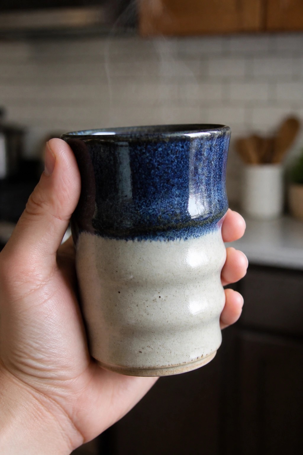 Hand holding steaming two-toned blue and beige ceramic mug in kitchen