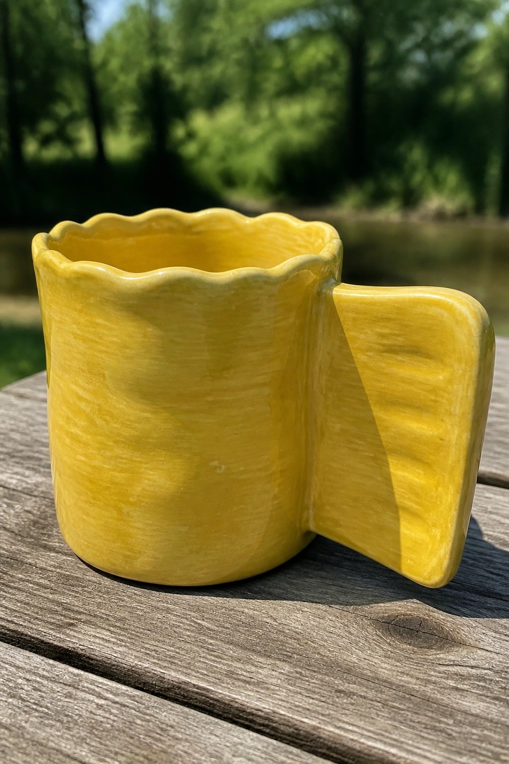 Yellow ceramic mug with scalloped rim and rectangular handle on wooden table