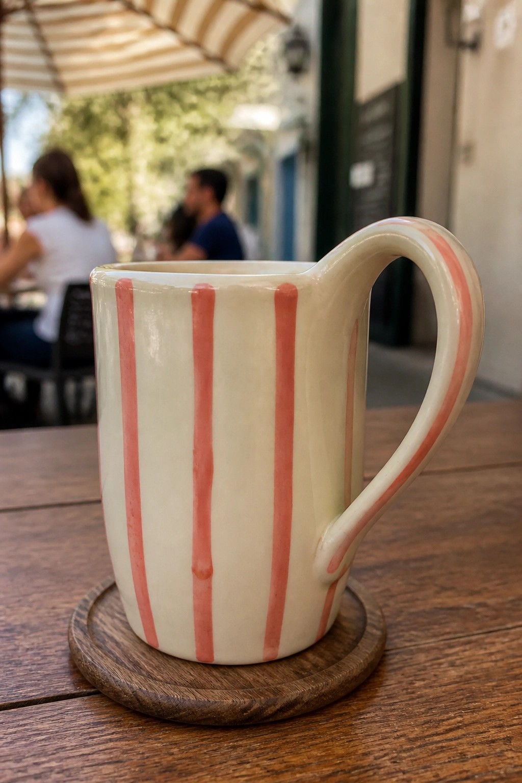 A white ceramic mug with vertical pink stripes sits on a wooden coaster.