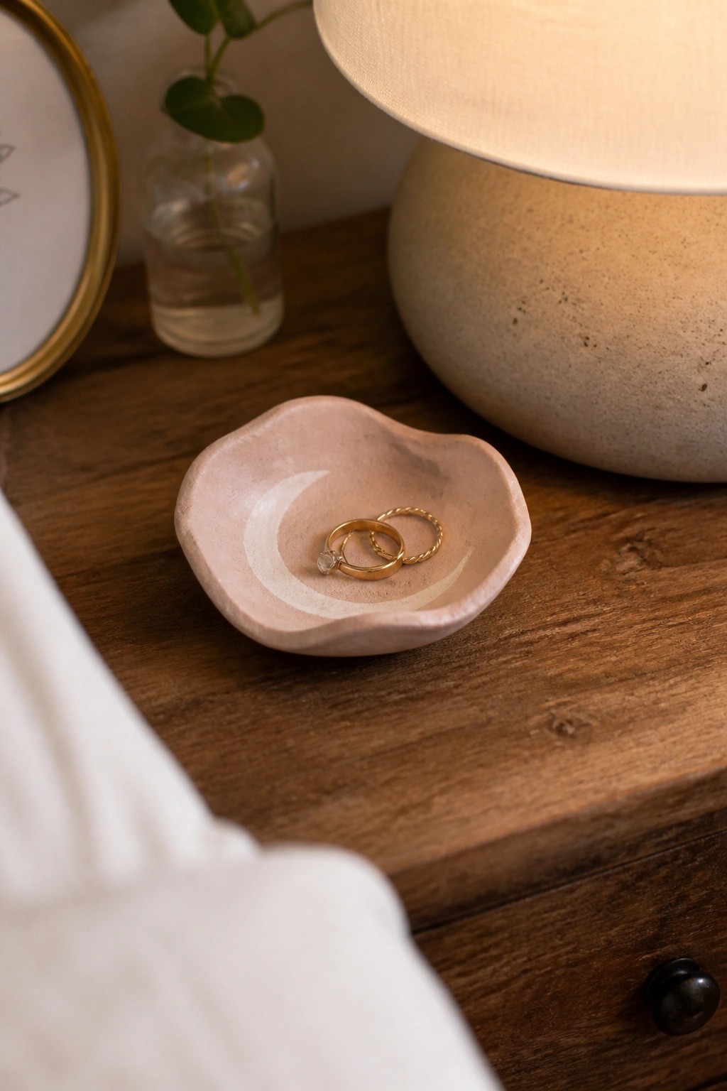 Two gold rings in pink ceramic dish with white crescent moon on wood.