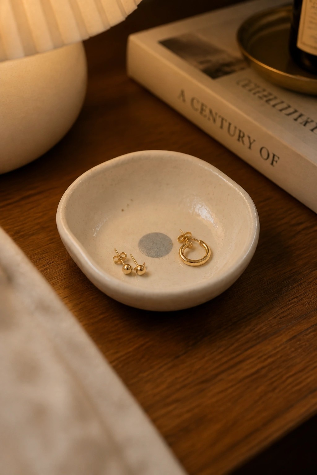 Gold stud and hoop earrings in a small white ceramic bowl on wood