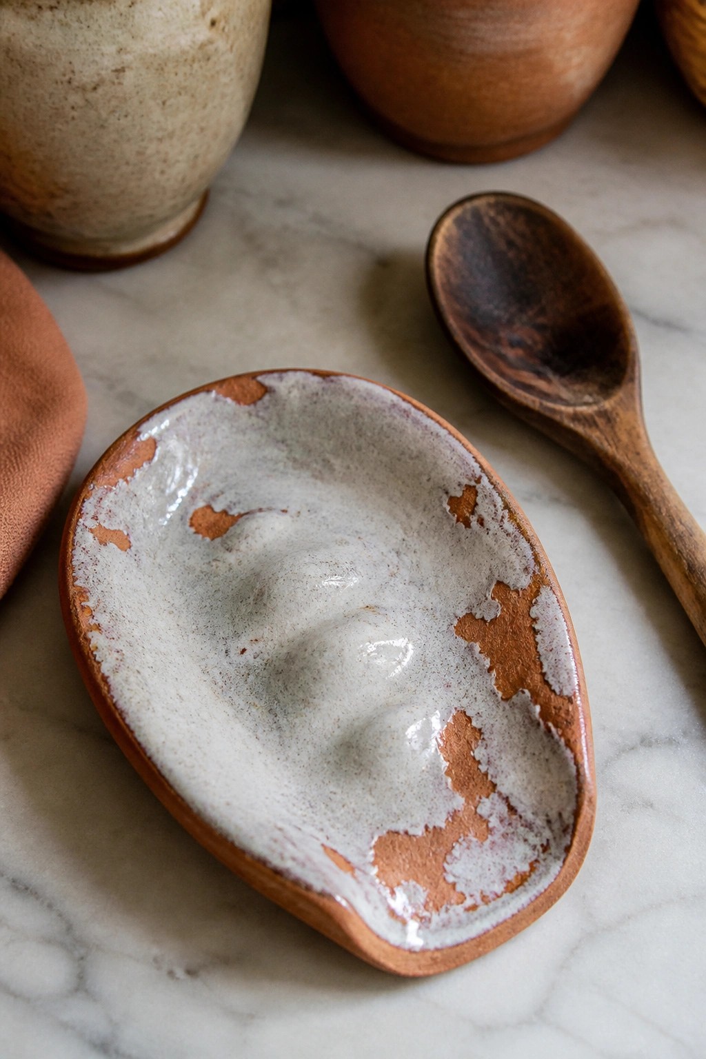 Rustic terracotta dish with chipped white glaze beside wooden spoon on marble