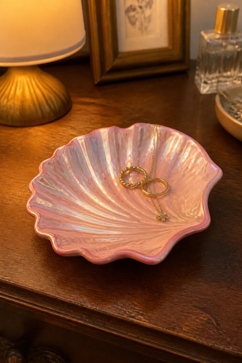 Pink iridescent seashell bowl with gold rings and necklace on wooden table