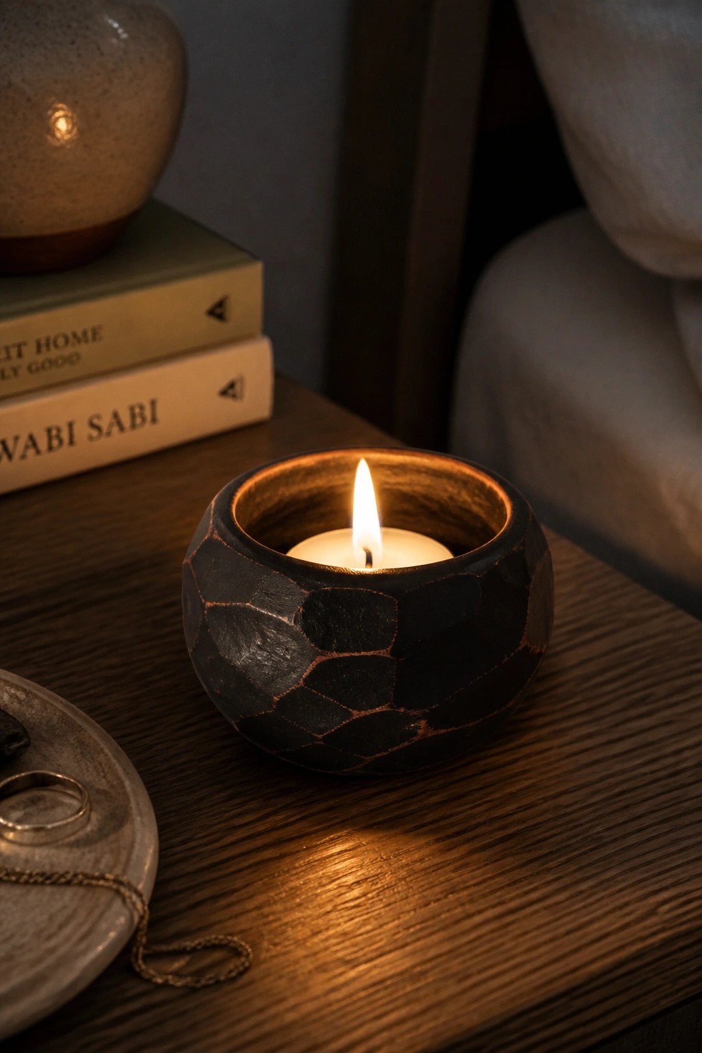 Lit candle in a dark mosaic holder on wooden table beside stacked books.