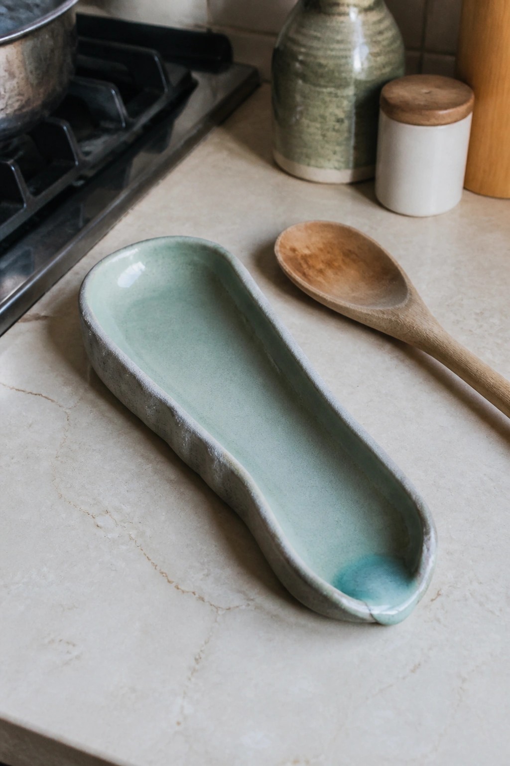 Light green ceramic tray and wooden spoon on marble kitchen counter