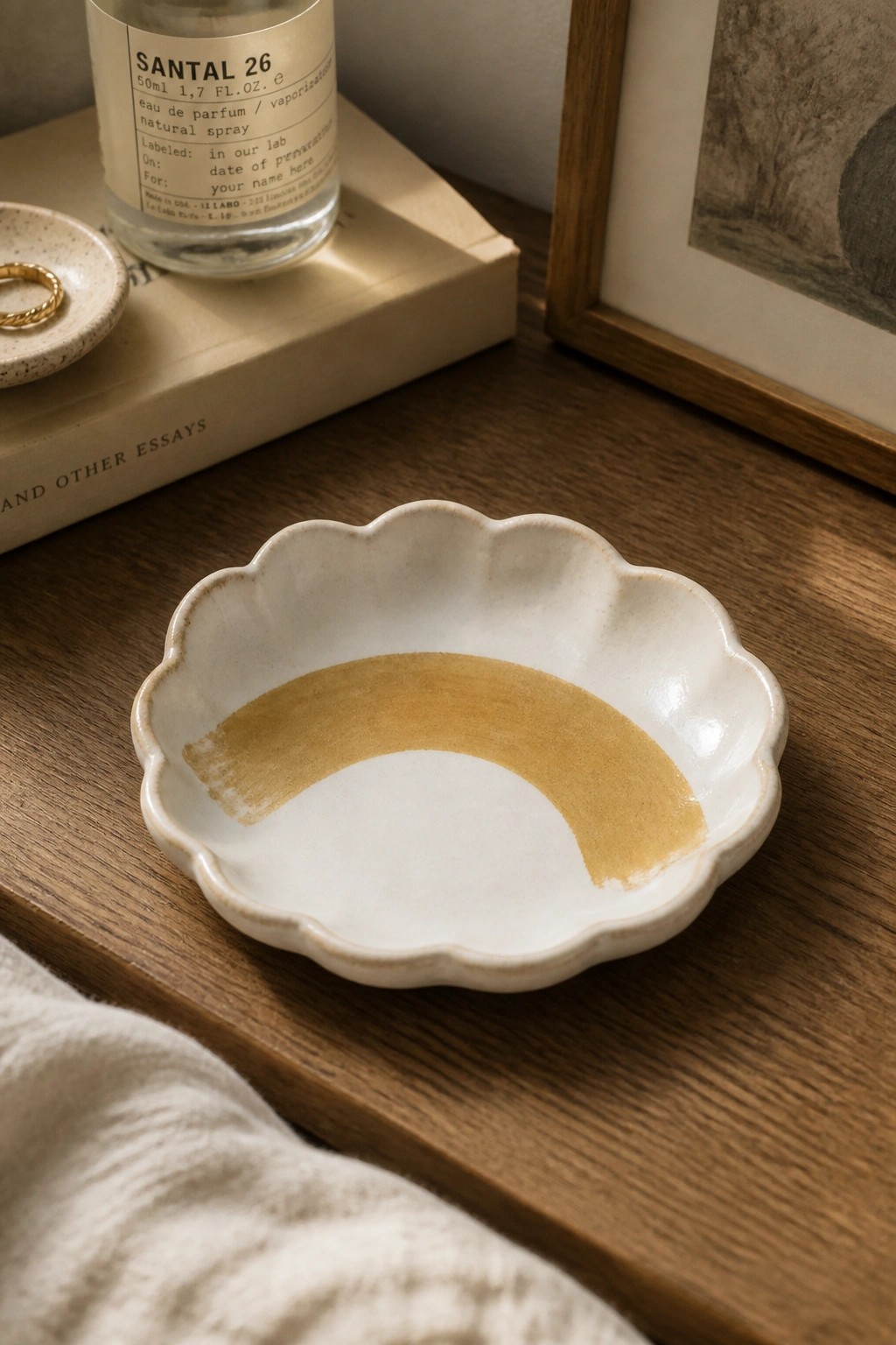 White scalloped ceramic bowl with golden arc on wooden table beside perfume bottle