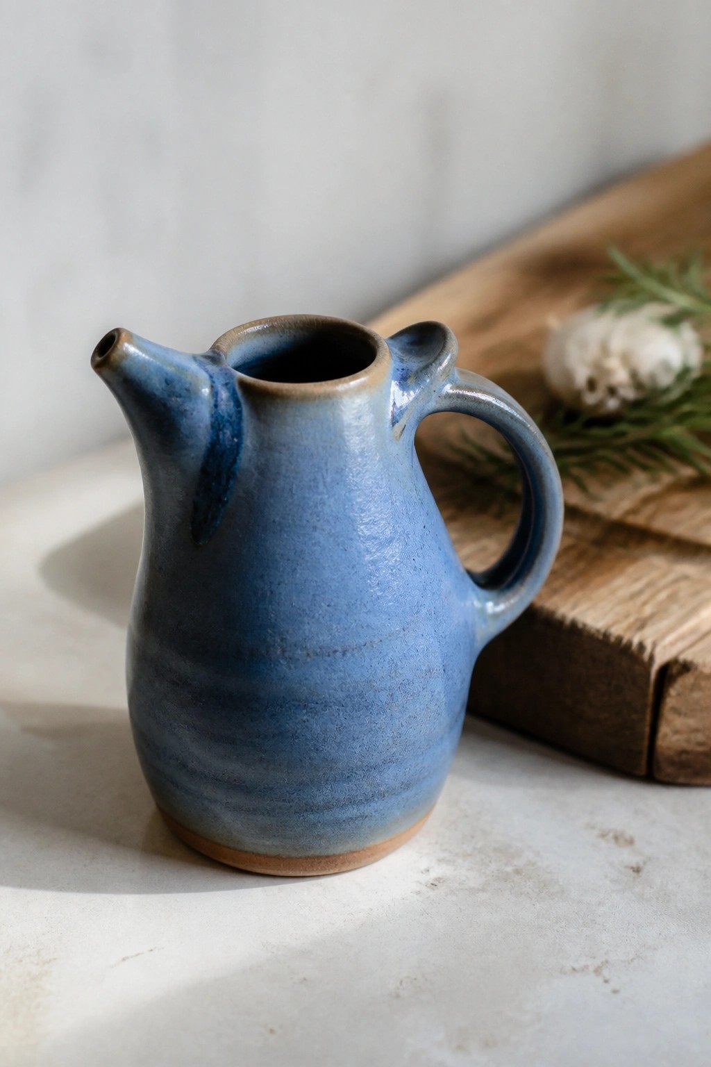 Blue ceramic pitcher with handle and spout near wooden board with garlic and rosemary