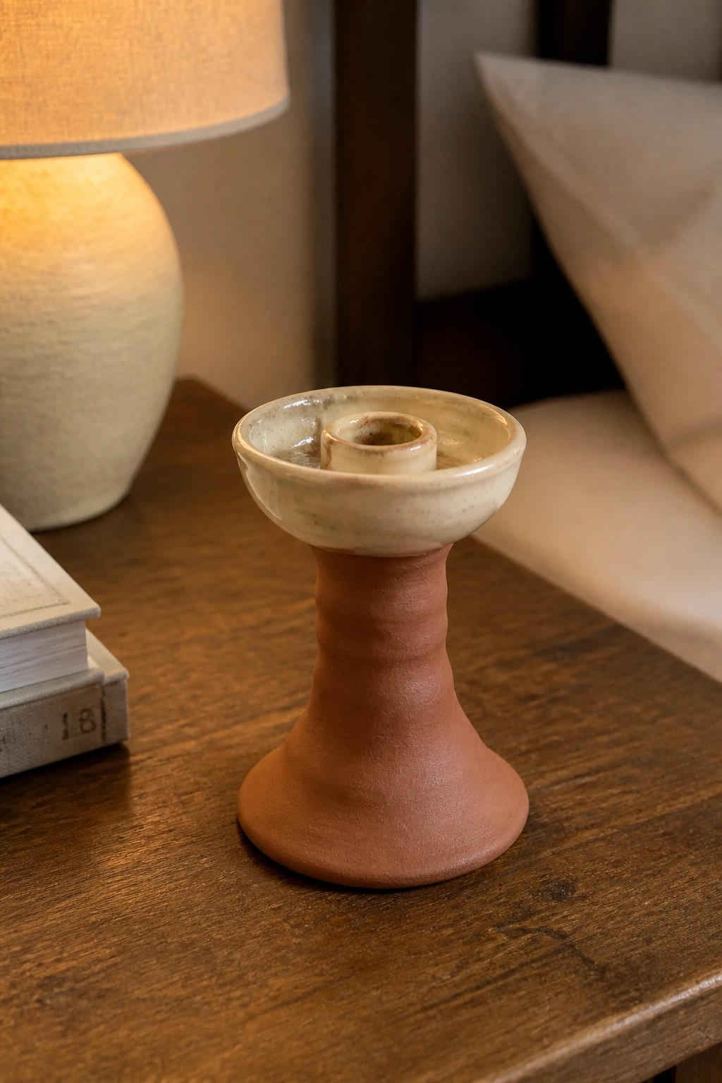 Ceramic candlestick with terracotta base and cream top on wooden table near lamp