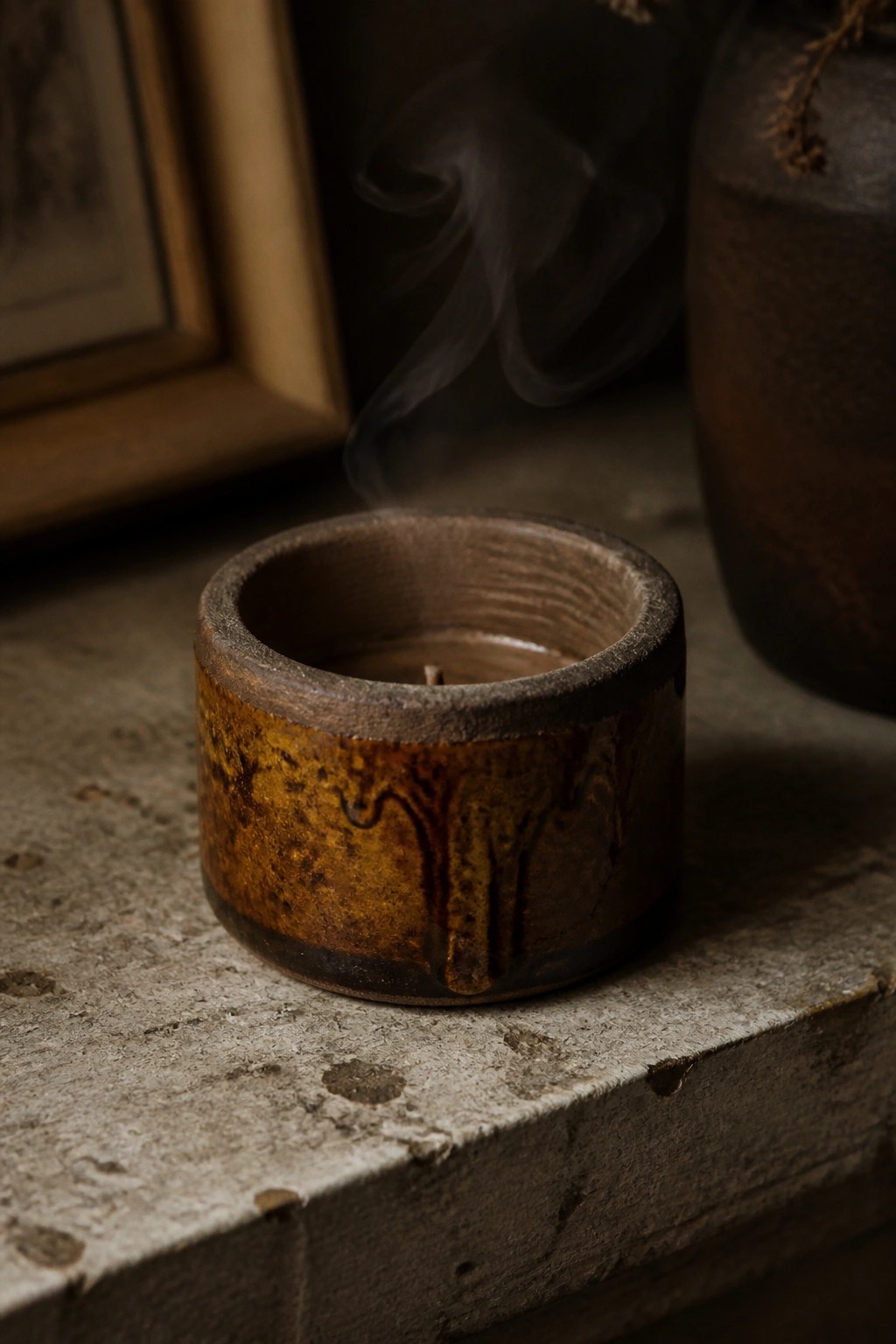 Rustic ceramic candle holder with smoke rising on textured concrete surface