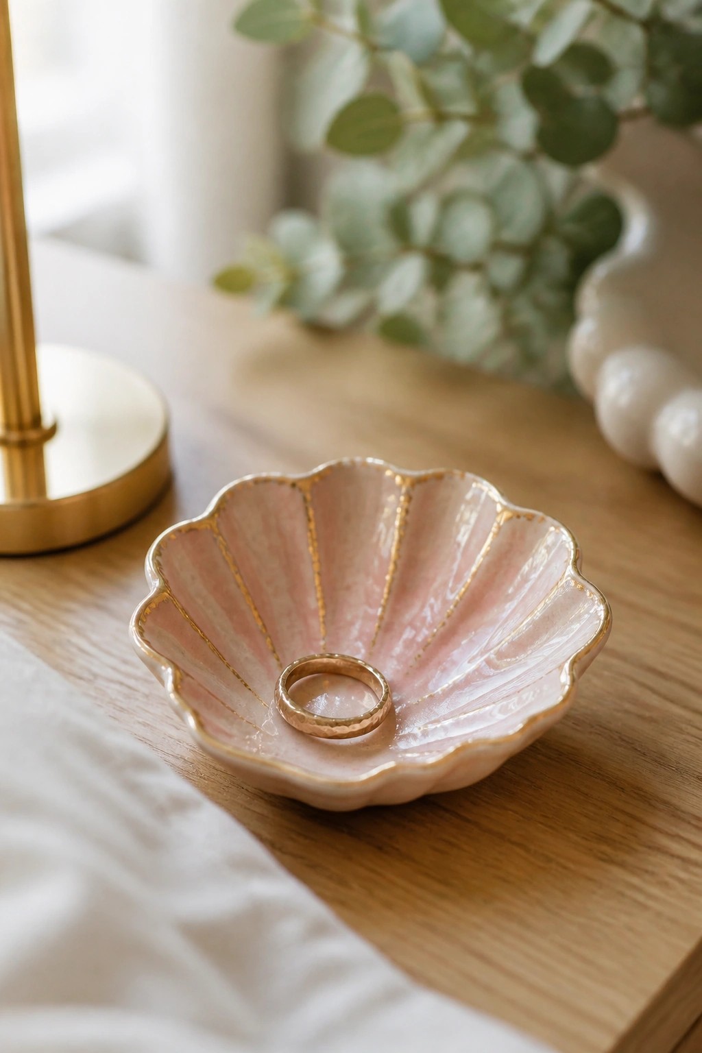 Pink shell-shaped ceramic dish with gold accents holding a gold ring on wood