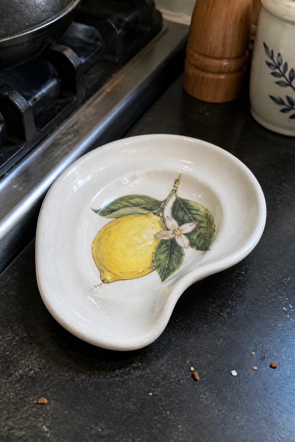 White ceramic spoon rest with yellow lemon and green leaves on dark counter