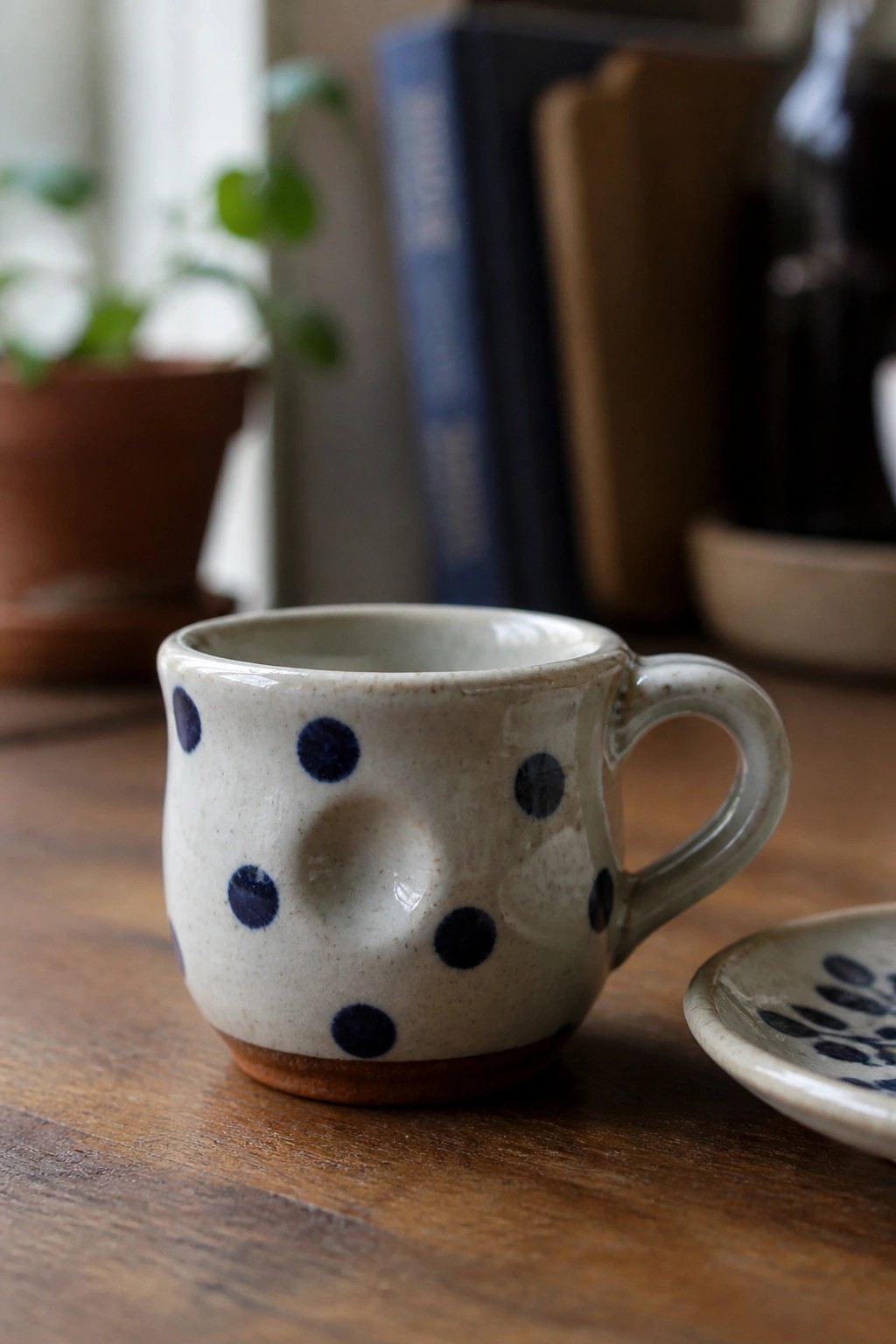 Polka-dotted ceramic mug with handle on wooden table beside saucer