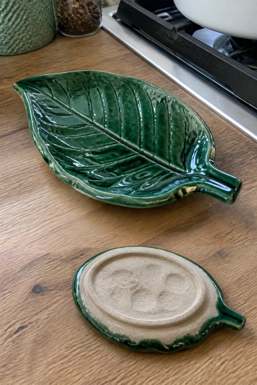 Green leaf-shaped ceramic dish and unglazed base on wooden kitchen counter.