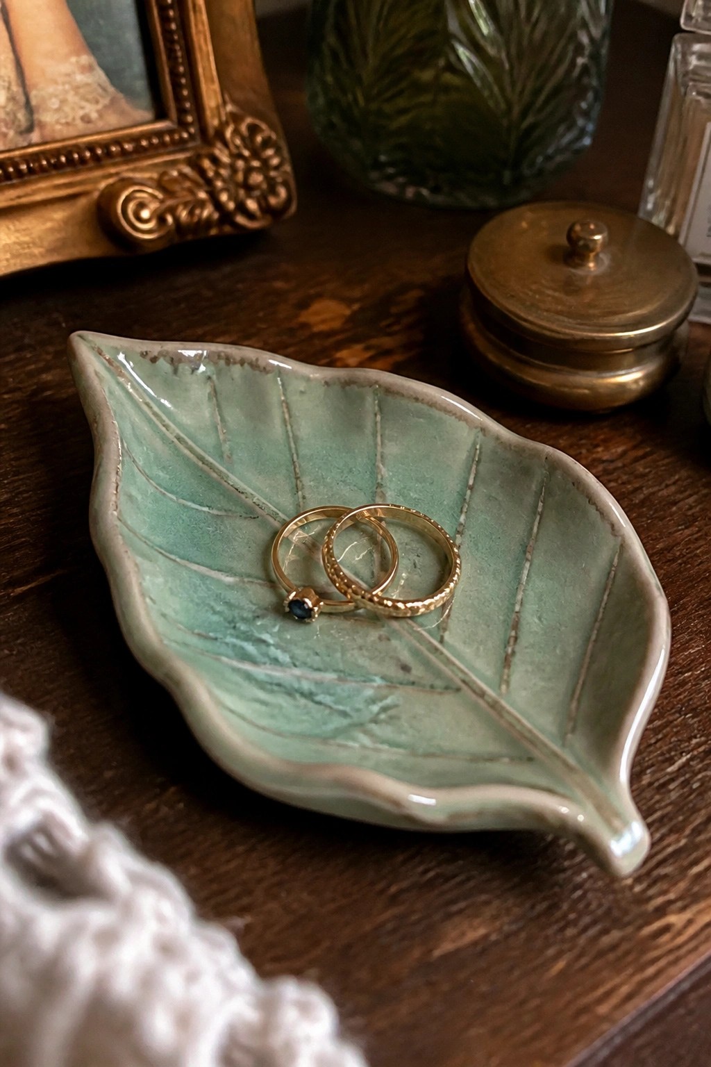 Two gold rings in a mint green ceramic leaf dish on dark wood.